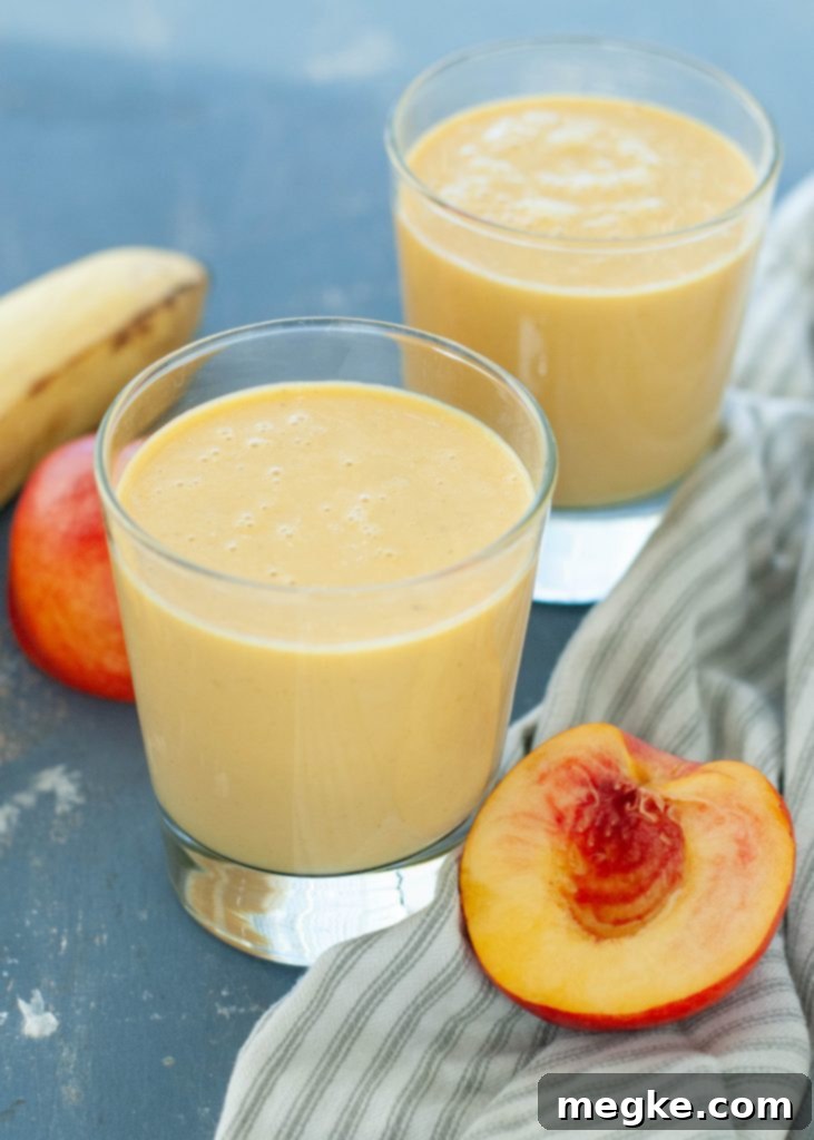 Peachy Dairy-Free Protein Boost 61 dairy-free peach protein smoothie in two glasses with fruit around it